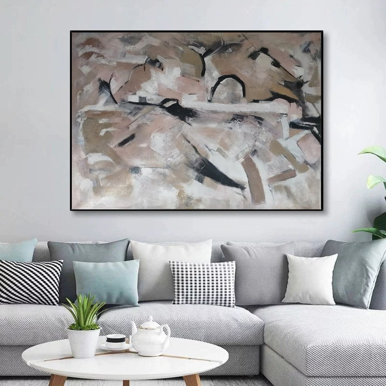 May include: Abstract painting with a black frame. The painting features a mix of beige, brown, and white paint with black accents.