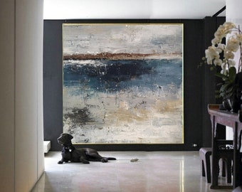 Puede incluir: Gran pintura abstracta con marco dorado. La obra presenta un paisaje texturizado con tonos de azul, gris, marrón y blanco. Un perro negro está tumbado en el suelo frente a la pintura.