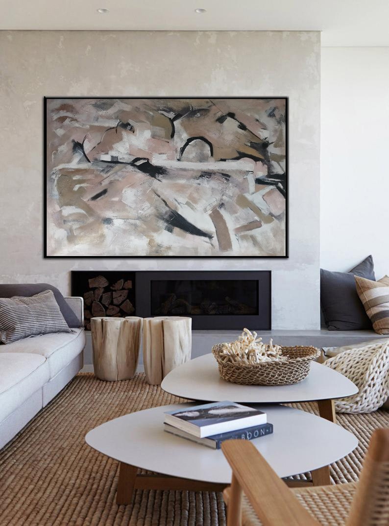 May include: Abstract painting in shades of brown, pink, and white with black accents. The painting is framed in a black frame and is hanging on a wall above a fireplace. The fireplace is made of stone and has a black mantel. There are two wooden stools in front of the fireplace.