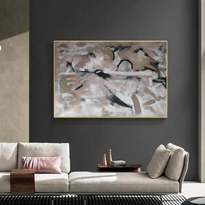 May include: Abstract painting with a gold frame. The painting features a mix of brown, beige, and white paint with black accents. The painting is displayed on a wall in a modern living room.