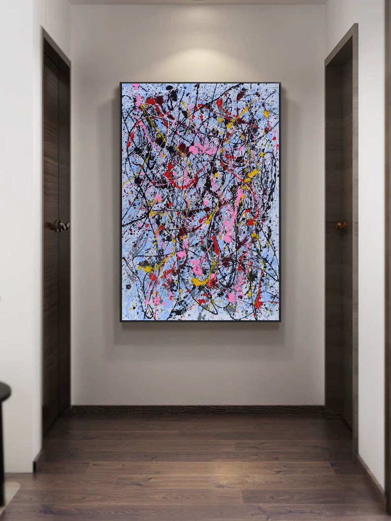 Puede incluir: Pintura abstracta con salpicaduras de pintura negra, blanca, rosa, roja y amarilla sobre un fondo azul claro. La pintura est&aacute; enmarcada en negro y colgada en una pared blanca.
