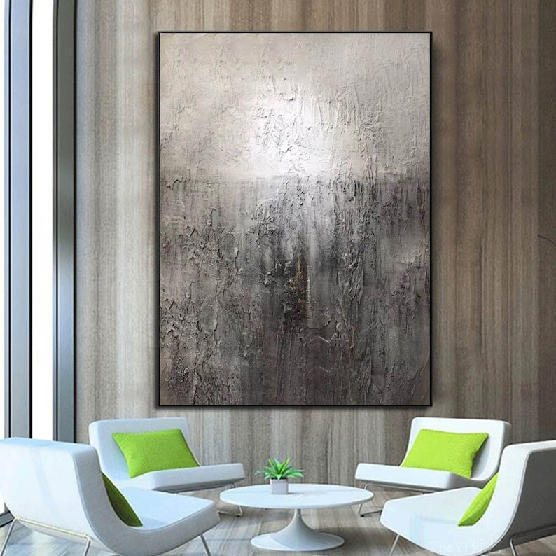 May include: Abstract painting with a textured, gray and white color scheme. The painting is framed and hanging on a wall in a modern living room setting.