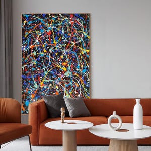 Puede incluir: Una gran pieza de arte mural rectangular con un fondo negro cubierto por un patrón denso y caótico de pintura salpicada en tonos vibrantes de azul, rojo, amarillo, naranja, blanco y verde, enmarcada en un borde fino de madera clara.