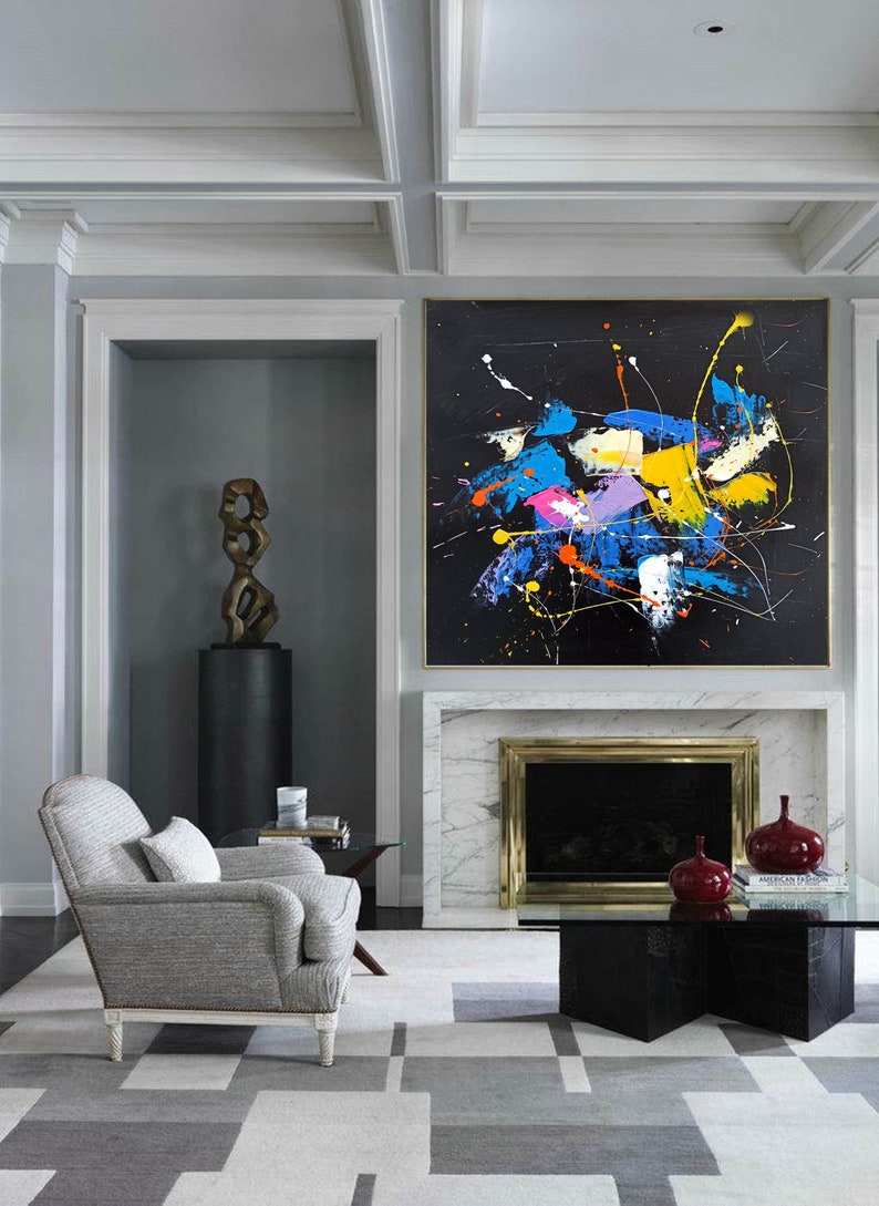 May include: A modern living room with a fireplace and a large abstract painting above it. The painting features a black background with splashes of blue, yellow, pink, and orange paint. A gray armchair sits in front of the fireplace, and a glass coffee table sits in front of the armchair.