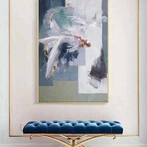 Puede incluir: Un banco tapizado en terciopelo azul con estructura de metal dorado. El banco est&aacute; delante de una pared blanca con una pintura abstracta enmarcada de un pez blanco con detalles dorados y rojos.