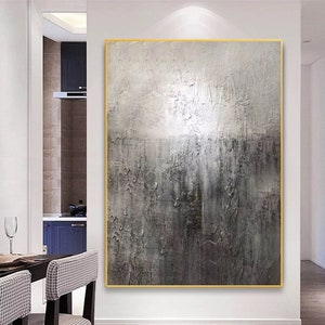 May include: Abstract painting with a textured, gray and white color scheme. The painting is framed in a gold frame and is hanging on a white wall.