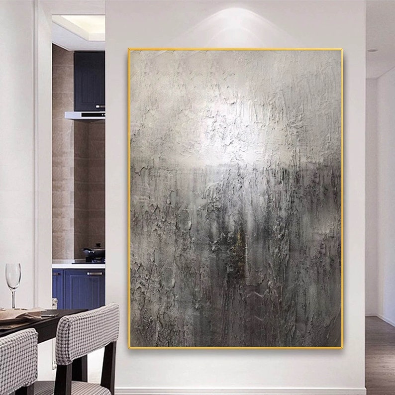 May include: Abstract painting with a textured, gray and white color scheme. The painting is framed in a gold frame and is hanging on a white wall.