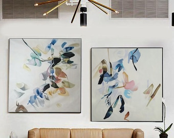 May include: Two abstract paintings with a white background and colorful shapes in shades of blue, pink, yellow, and brown. The paintings are framed in black and hung on a white wall.