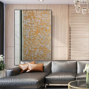 K&ouml;nnte beinhalten: Abstrakter Kunstdruck mit wei&szlig;em Hintergrund und goldenen Linien. Der Druck ist gerahmt und h&auml;ngt an einer Wand in einem Wohnzimmer.