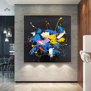 Abstract painting with splashes of blue, yellow, pink, and orange paint on a black background.