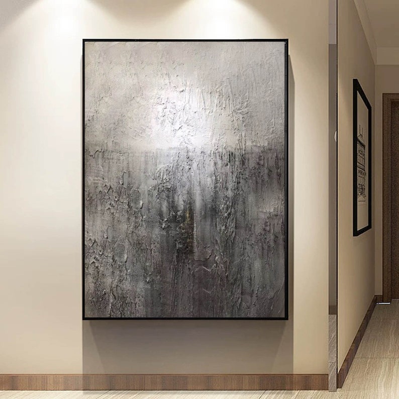 May include: Abstract painting with a textured, gray and white color scheme. The painting is framed in black and hangs on a wall.