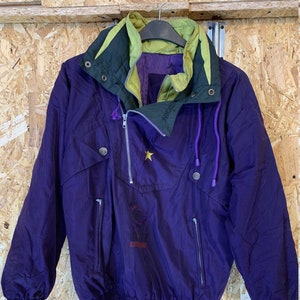 Puede incluir: Chaqueta anorak morada vintage con cuello alto y cremallera. La chaqueta presenta un emblema de estrella amarilla y el texto "HIGHLAND OUTDOOR". El cuello es verde y amarillo, con cordones morados y dos bolsillos delanteros.