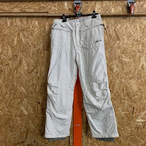 Puede incluir: Pantalones de esqu&iacute; color blanco roto con m&uacute;ltiples bolsillos y rodillas reforzadas colgados de una percha negra. Los pantalones tienen cierre de cremallera y un logotipo en la parte superior de la pierna izquierda. Hechos de material resistente al agua.