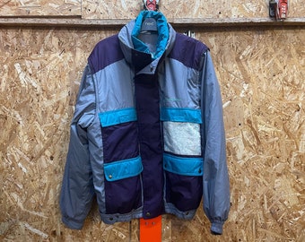 May include: A vintage jacket in shades of grey, purple, and teal, hanging against a wood-panelled wall. The jacket features a high collar, multiple pockets, and the brand name "Next" on the label. A retro style.
