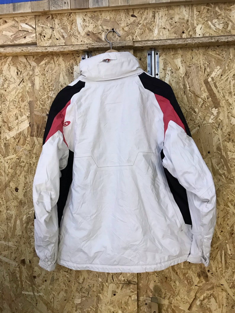 Puede incluir: Chaqueta de invierno blanca y negra con detalles en rojo. La chaqueta est&aacute; colgada de un gancho met&aacute;lico. Tiene un cuello alto y cierre de cremallera. Fabricada con material resistente al agua.