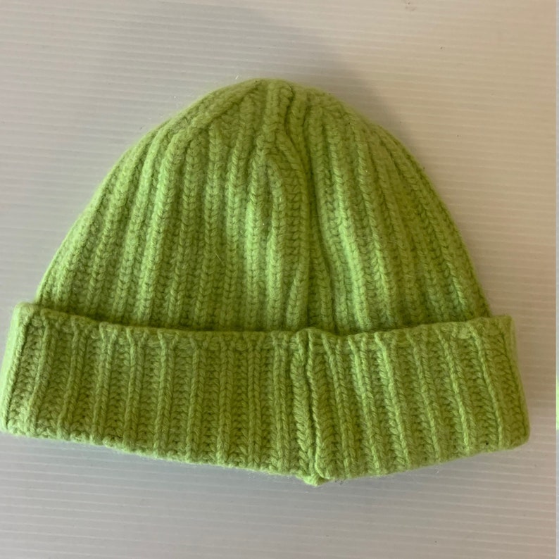 May include: A lime green knit beanie hat with a ribbed texture. The hat has a folded brim and is made of a soft, warm material. This winter hat is a stylish accessory for cold weather.