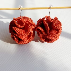 May include: A pair of orange crocheted earrings hanging from a wooden dowel rod. The earrings are round and have a ruffled texture.