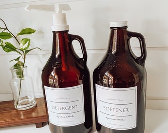 May include: Two brown glass bottles with white pump tops and labels. The bottle on the left says "HAND POURED - DETERGENT - Signature Collection". The bottle on the right says "HAND POURED - SOFTENER - Signature Collection".