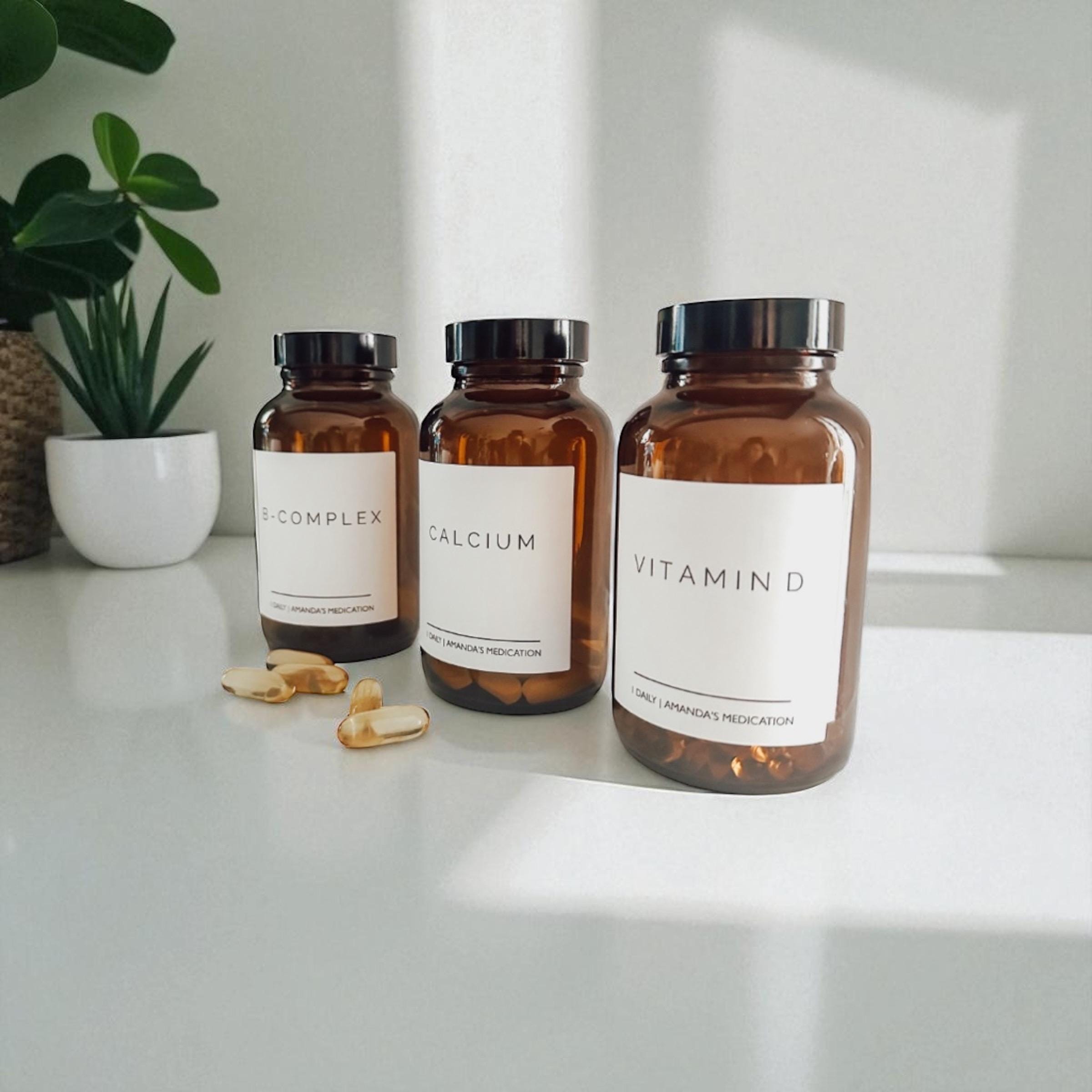 Trio de frascos de vitaminas sobre uma superfície clara, com cápsulas ao lado, lembrando que suplemento exige leitura de rótulo e contexto