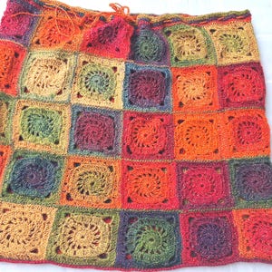 Könnte beinhalten: Ein farbenfroher, handgefertigter Häkelrock mit einem Patchwork-Design aus quadratischen Motiven. Der Rock zeigt eine lebendige Farbpalette aus Rot-, Orange-, Grün- und Lilatönen. Die Quadrate haben ein Spiralmuster in der Mitte und sind miteinander verbunden.