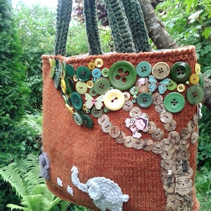 May include: A brown knitted tote bag with a tree design made of buttons and other embellishments. The bag has a green crocheted strap and features a small elephant and owl design.