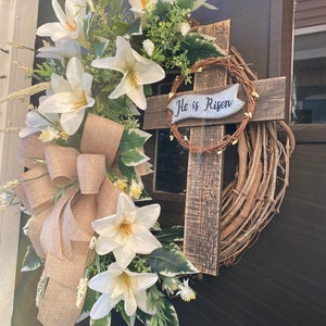 May include: A white floral wreath with a wooden cross and the text "He is Risen" on a brown door.