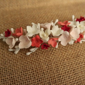 以下が含まれることがあります： 白、ピンク、赤の花が付いた花のヘアコーム。コームは金属製で、繊細なデザインです。