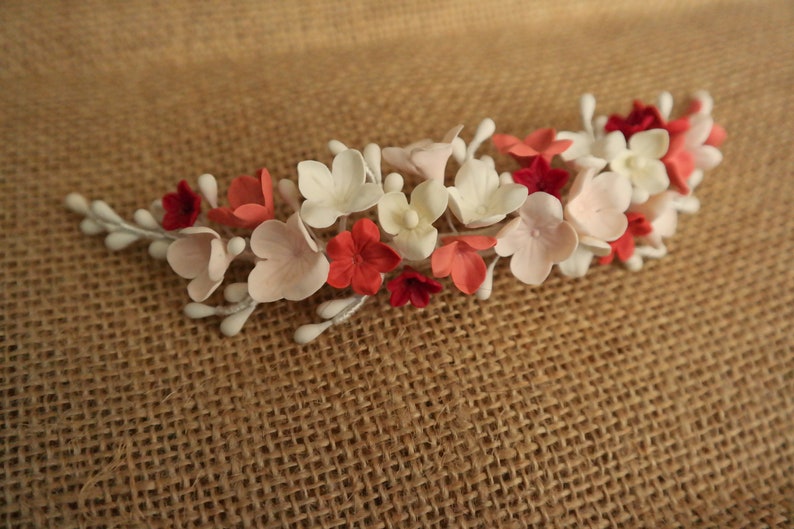 以下が含まれることがあります： 白、ピンク、赤の花が付いた花のヘアコーム。コームは金属製で、繊細なデザインです。
