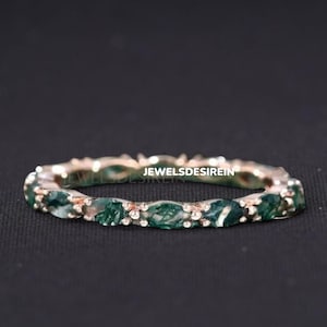 Puede incluir: Una banda de eternidad de oro rosa con una fila de piedras preciosas verdes. La banda está engastada con pequeñas piedras de forma ovalada.