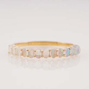 May include: A delicate gold band ring with a row of white opal stones.
