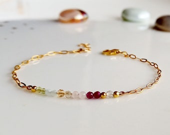 May include: A gold chain bracelet with a row of colourful gemstone beads. The beads are green, blue, brown, pink, and red.