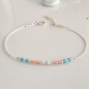May include: A delicate silver chain bracelet with a row of small turquoise, peach, and white beads.