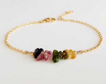 May include: A gold chain bracelet featuring a row of small, colourful gemstones. The gemstones are in shades of pink, green, and yellow.
