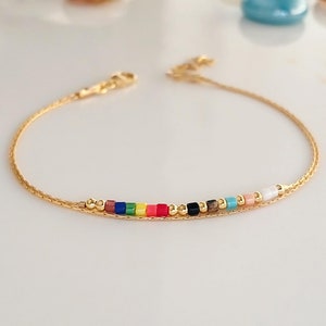 Könnte beinhalten: Ein goldenes Kettenarmband mit einer Reihe bunter quadratischer Perlen. Die Perlen sind in einem Regenbogenmuster angeordnet.