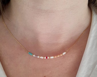 May include: A delicate gold necklace featuring a row of small, colorful beads. The beads include turquoise, pink, white, red, and gold, strung along a fine gold chain. The necklace is worn around the neck.