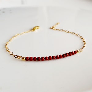 May include: A delicate gold chain bracelet with a row of small, red beads.