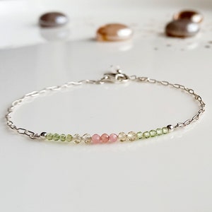 May include: A delicate silver chain bracelet with a row of small green, yellow, and pink gemstone beads.