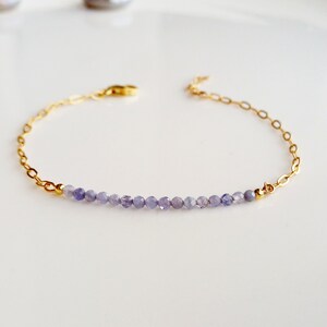May include: A delicate gold chain bracelet with a row of small, light purple amethyst beads.