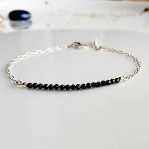 May include: A delicate silver chain bracelet with a single row of black beads.