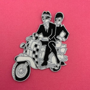 May include: Black and white embroidered patch of two figures wearing hats and sunglasses riding a scooter.