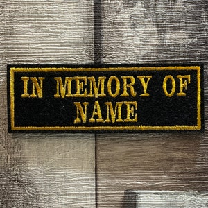 May include: Black rectangular patch with gold embroidered text that reads "In Memory Of NAME".