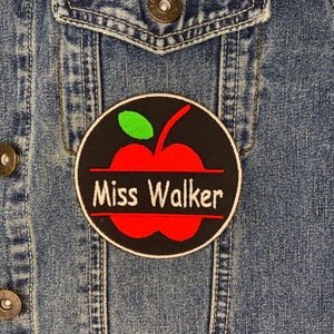 May include: A red apple with a green leaf on a black circle with a white border. The text "Miss Walker" is written on a white banner across the apple.
