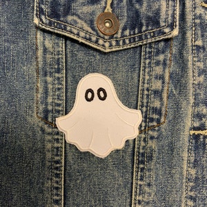 May include: A white ghost patch with black eyes sewn onto a blue denim jacket.