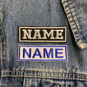 May include: Two embroidered patches with the word "NAME" in white lettering. The top patch has a black background and white stitching. The bottom patch has a blue background and white stitching.