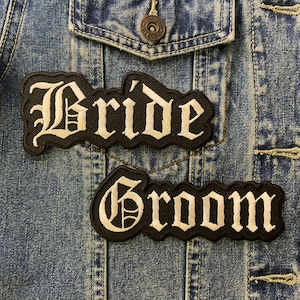 May include: Two black fabric patches with white lettering. The top patch says "Bride" and the bottom patch says "Groom".