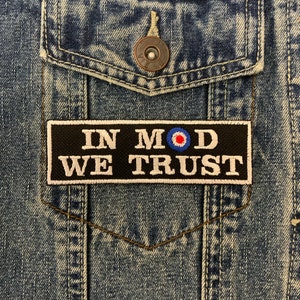 May include: Black and white embroidered patch with the text "In Mod We Trust" and a red, white and blue target symbol. The patch is sewn onto a blue denim jacket.