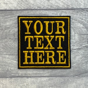 May include: Black square patch with a gold embroidered border and the text "YOUR TEXT HERE" in gold.