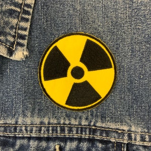 May include: A yellow and black radiation symbol patch sewn onto a blue denim jacket.