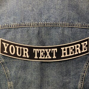 May include: A black and white embroidered patch with the text "YOUR TEXT HERE" in a curved shape. The patch is sewn onto a blue denim jacket.