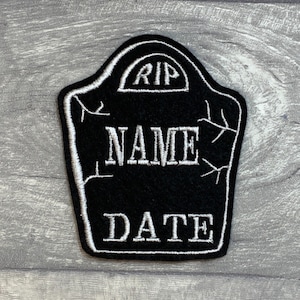 May include: Black felt tombstone-shaped patch with white embroidery. The patch reads "RIP" in a rounded arch at the top, "NAME" in the centre, and "DATE" at the bottom.